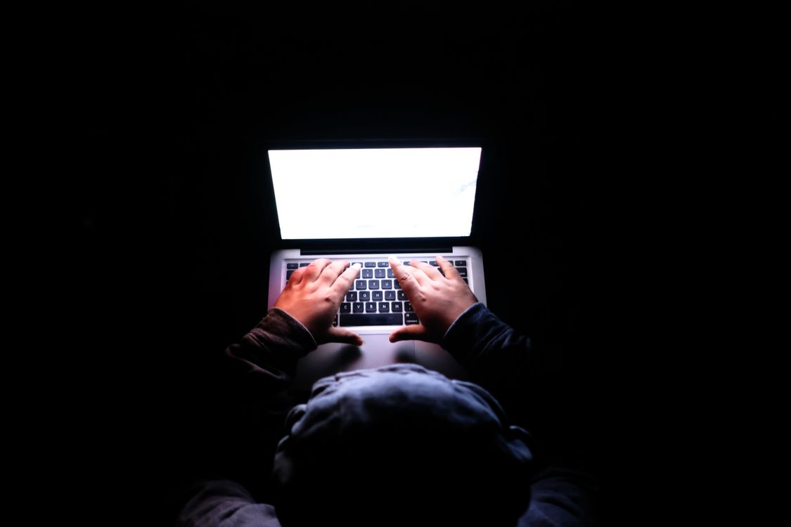 A person typing on a laptop in a dark room — attackers automate scanning for unpatched instances