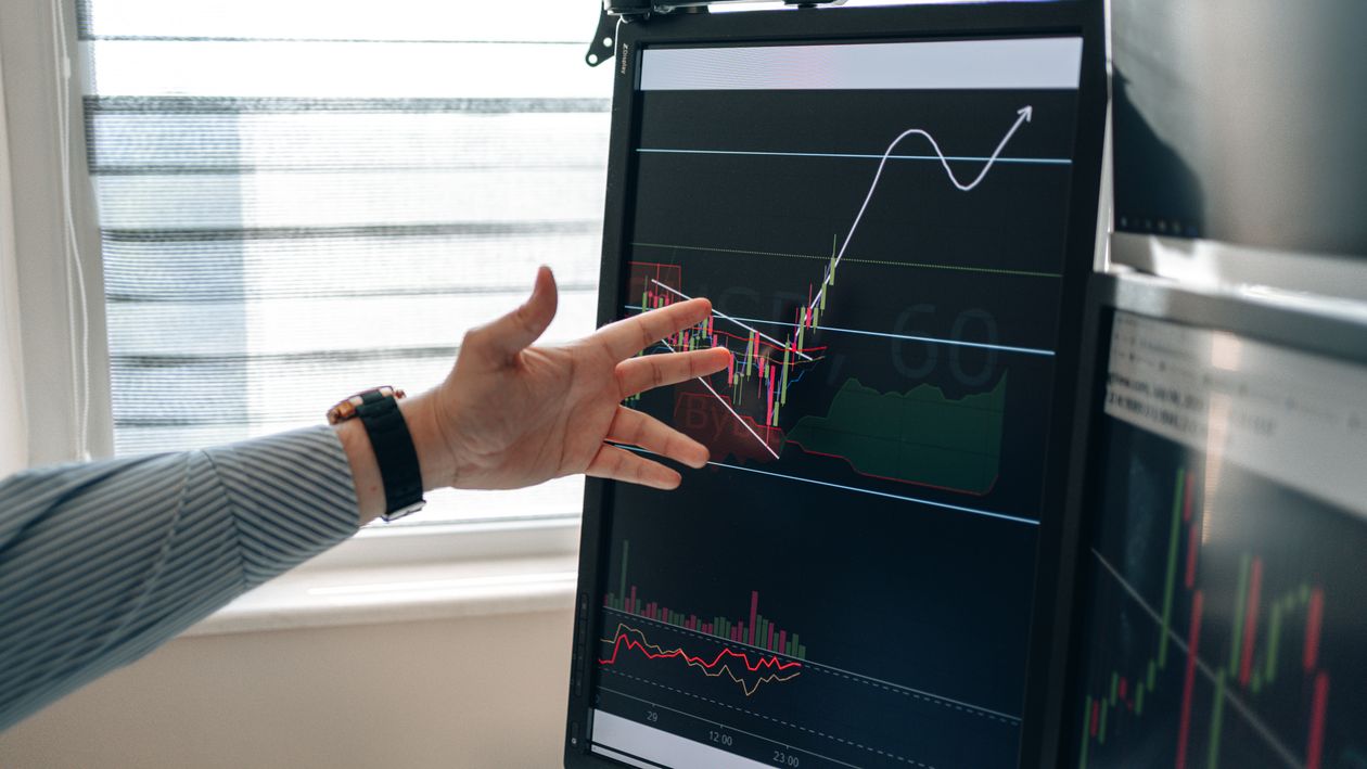 Person's hand pointing at a candlestick stock chart on a monitor