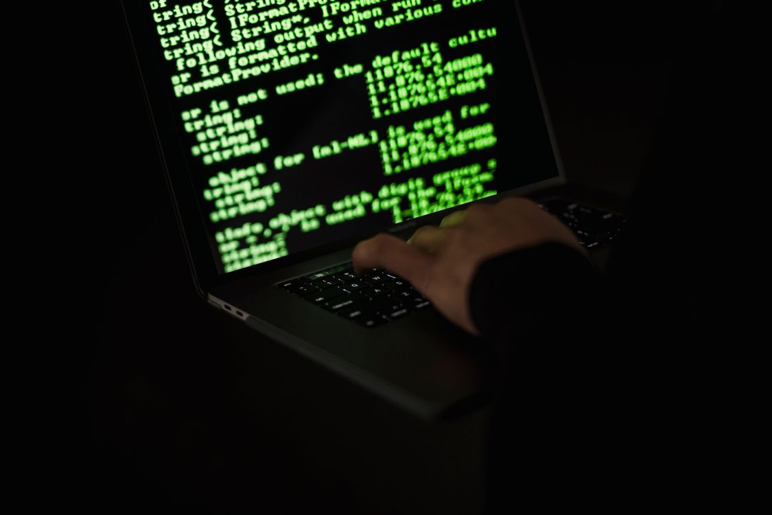 A hooded figure typing at a laptop with data streams on screen — illustrating the threat actor behind the Tensorlake npm compromise