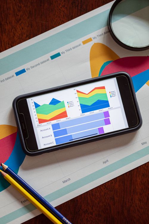 A smartphone showing colorful analytics charts on top of printed marketing reports — when engagement becomes the billable event, the measurement layer is the invoice